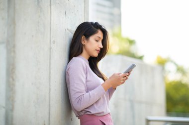 Cep telefonuyla duvara yaslanan genç bir kadının yan portresi.