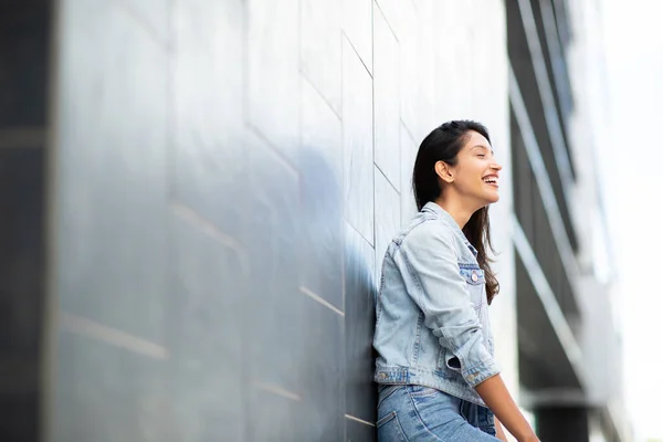 Side portrait of happy young woman leaning against wall outdoors
