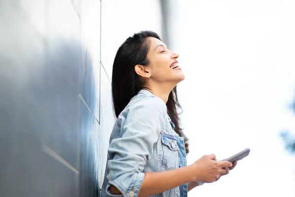 壁に携帯電話を持つ笑っている女性のサイドポートレート — ストック写真