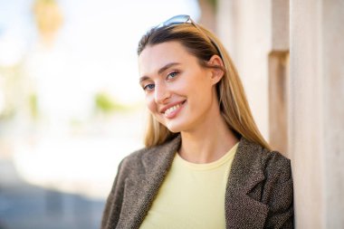 Dışarıdaki duvara yaslanırken poz veren güzel bir genç kadının portresi.