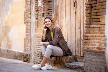 Güzel genç bir kadın cep telefonuyla konuşuyor ve dışarıda otururken gözlerini kaçırıyor. 