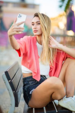 Güzel, şık, genç bir bayan cep telefonuyla selfie çekiyor. 