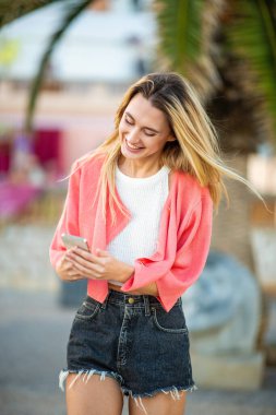 Açık havada cep telefonu kullanan, şortlu, şık, genç, sarışın bir kadın.