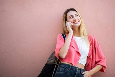 Pembe arka planda cep telefonuyla konuşan gülümseyen sarışın kadının portresi. 