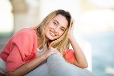 Açık hava duvarına yaslanmış gülümseyen genç bir kadının portresi.