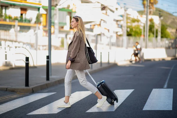 Full body side portrait of woman crossing the street with travel bag
