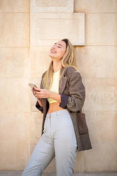 Радостная Дама Развлекается Пользуясь Мобильным Телефоном Опираясь Наружную Стену — стоковое фото