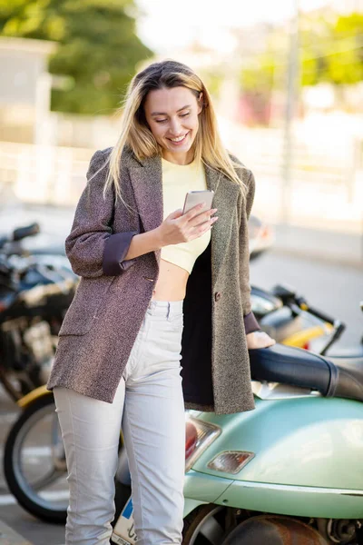 Mujer Joven Sonriente Usando Teléfono Móvil Mientras Apoya Scooter Pie —  Fotos de Stock