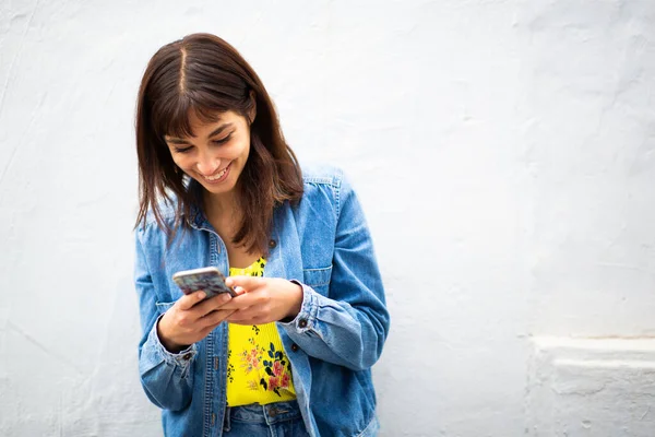 Портрет Улыбающейся Молодой Женщины Прислонившейся Белой Стене Использующей Мобильный Телефон — стоковое фото