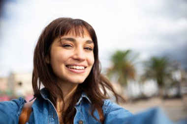 Dışarıda selfie çeken neşeli genç bir kadının portresi.
