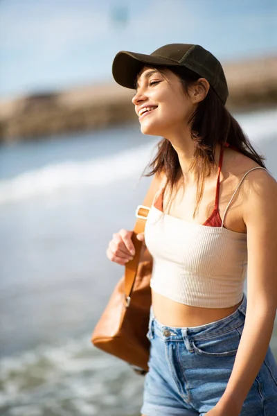 バッグと笑顔でビーチを歩く美しい若い女性の肖像画 — ストック写真