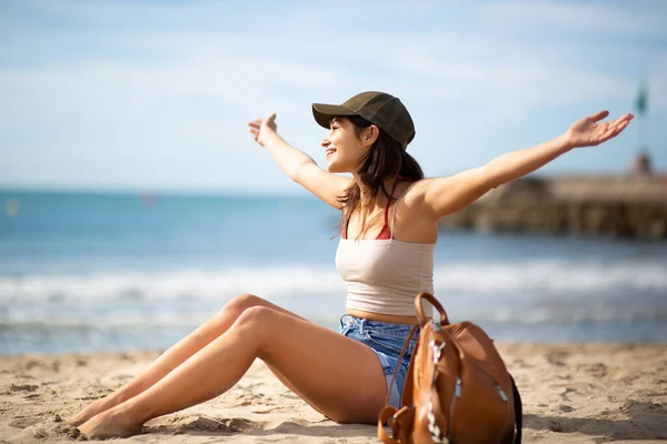 腕を伸ばしてビーチでリラックスした美しい若い女性のサイドポートレート — ストック写真