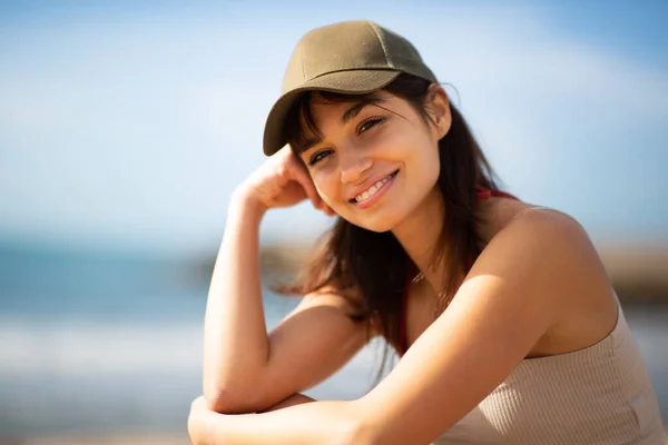 坐在海滩上的戴着帽子的年轻漂亮女子的特写 在镜头前显得很轻松 — 图库照片