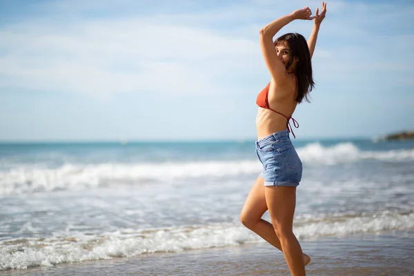 腕を上げて海岸に立つ魅力的な若い女性の肖像画 — ストック写真