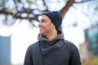 Siyah ceketli ve örgü şapkalı yakışıklı genç bir adamın portresi şehrin dışına bakıp gülümsüyor.