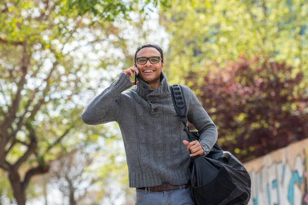 袋を外に歩いて携帯電話で話すと笑顔の若い男の肖像画 — ストック写真