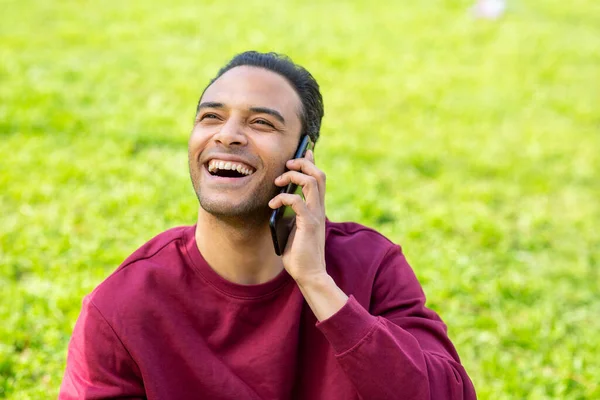 一个快乐的黑人年轻人坐在公园里用手机聊天的画像 — 图库照片