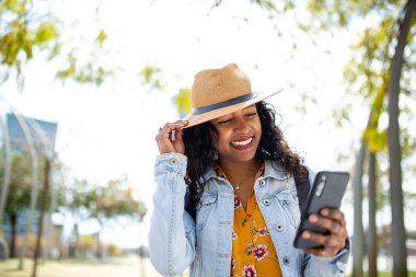 Dışarıda cep telefonuna bakıp gülümseyen güzel, Afro-Amerikan kadın portresi.