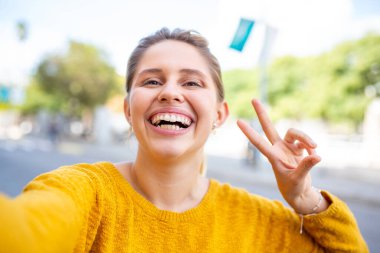 Güzel genç bir kadının yakın plan portresi barış işareti ile şehrin dışında selfie çekiyor.