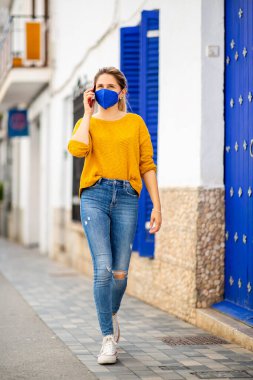 Şehirde yüz maskesi takmış cep telefonuyla konuşan genç bir kadının vücut portresi.