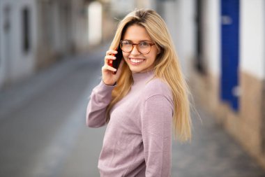 Çekici sarışın bir kadının portresi. Arkaya bakıyor ve şehirde cep telefonuyla konuşuyor.