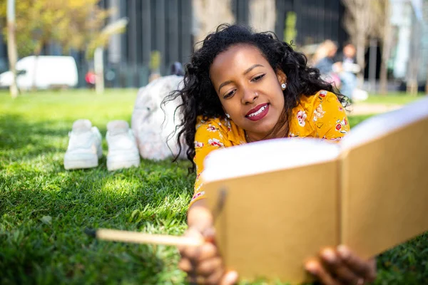 Genç Afro Amerikan Kadın Portresi Parkta Çimlere Uzanmış Kitap Yazıyor — Stok fotoğraf