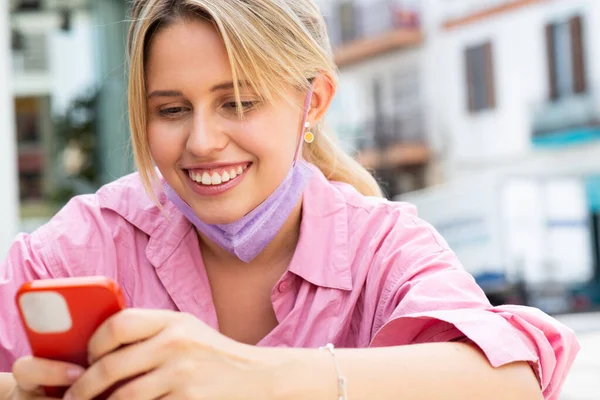 幸せな若い女性の肖像画は 外に座ってマスクと携帯電話でテキストメッセージ — ストック写真