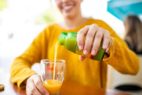 一位女士坐在室外咖啡店的瓶子里 将橙汁倒入玻璃杯 这是一个特写镜头 — 图库照片