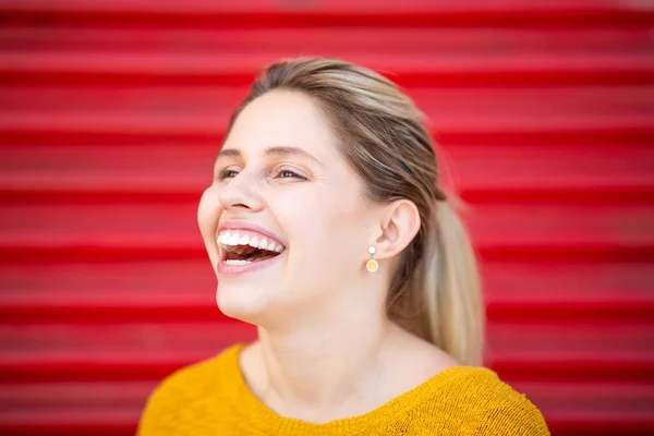 赤いシャッターの前で笑う若い女性のクローズアップポートレート — ストック写真