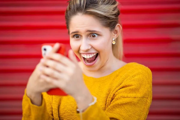 兴奋的年轻女子用红色快门窗看手机的特写 — 图库照片