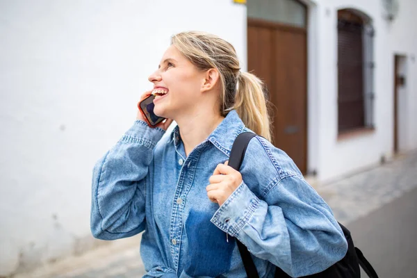 サイドビューの肖像画の明るい若い女性の袋で歩くと街の外の携帯電話で話す — ストック写真