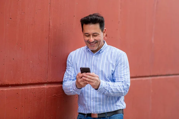 Kırmızı Duvara Yaslanan Cep Telefonu Kullanan Mutlu Olgun Bir Adamın — Stok fotoğraf
