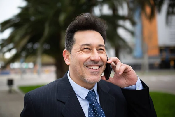 街の外に立って携帯電話で話している成熟したビジネスマンの笑顔のクローズアップ肖像画 — ストック写真