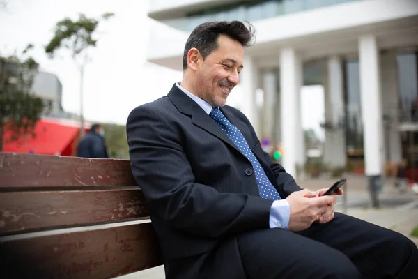 Πορτρέτο Του Χαμογελαστού Ώριμου Επιχειρηματία Κάθεται Στον Πάγκο Χρησιμοποιώντας Κινητό — Φωτογραφία Αρχείου