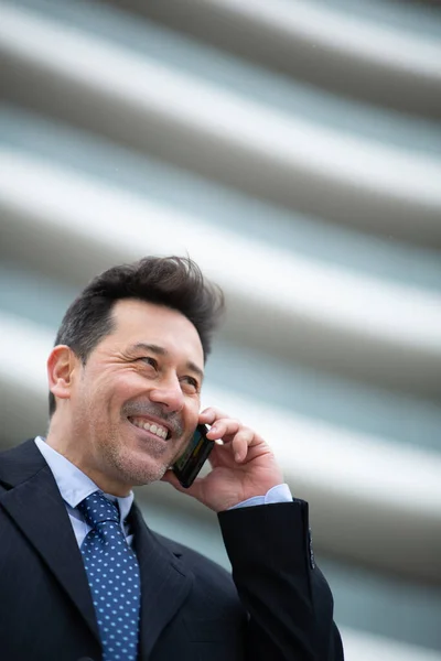 ビルの外に立って携帯電話で話している笑顔のビジネスマンのクローズアップ肖像画 — ストック写真