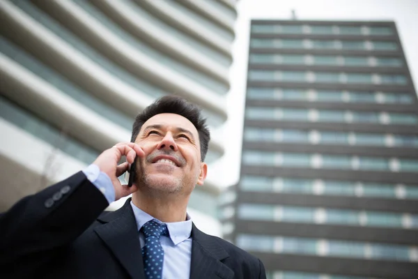 低い角度閉じますアップポートレートの幸せな成熟したビジネスマン立ってフロント背の高い建物で携帯電話で話して外 — ストック写真