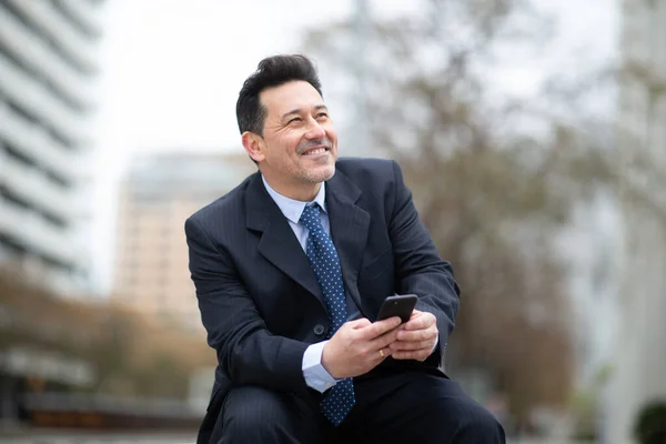 幸せな成熟したビジネスマンの肖像携帯電話で外に座って — ストック写真