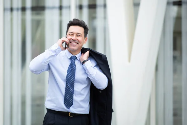 一个面带微笑 成熟的生意人背着外套在外面用手机聊天的画像 — 图库照片