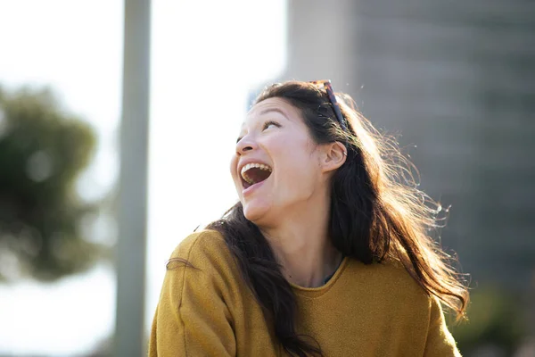 街の外に座っている興奮した若いアジア人女性のクローズアップポートレート離れて見て笑って — ストック写真