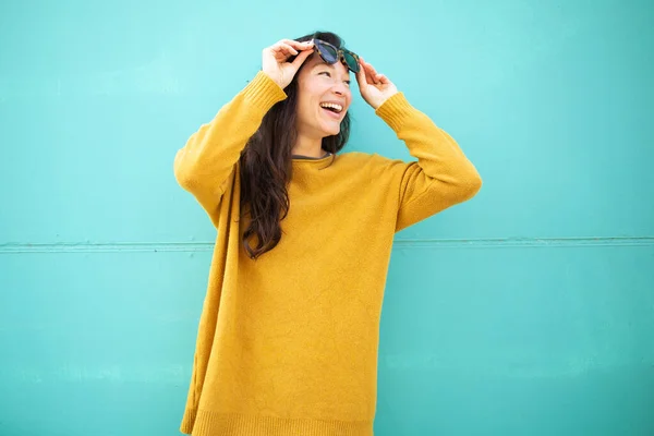 stock image Portrait of beautiful young woman holding her sunglasses looking away and smiling against green wall