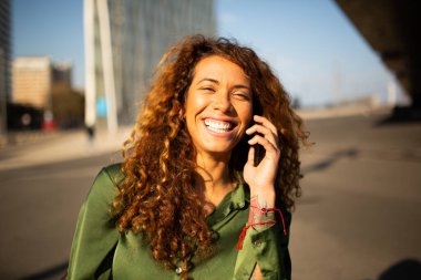 Şehirde cep telefonuyla konuşan gülümseyen genç bir kadının yakın portresi.