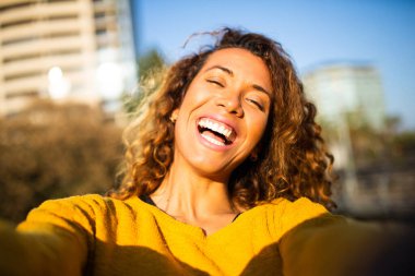 Dışarıdaki kıvırcık saçlı, neşeli Latin kadının selfie portresi.