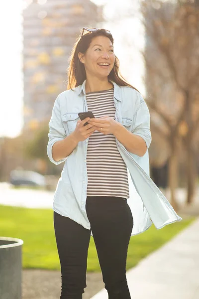 Portret Van Lachende Aziatische Vrouw Met Mobiele Telefoon Wegkijkend Stad — Stockfoto