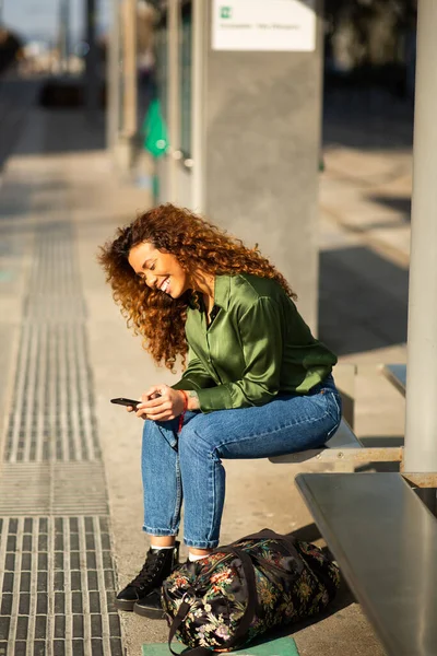 市内の公共交通機関を待っている間 陽気な若い女性の携帯電話でテキストメッセージのサイドポートレート — ストック写真