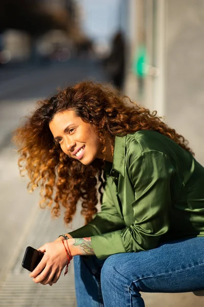 Портрет Счастливой Молодой Смешанной Расы Женщины Сидящей Снаружи Мобильным Телефоном — стоковое фото