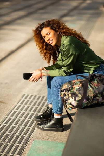 一个漂亮的年轻女子坐在外面 提着袋子望着别处的画像 — 图库照片