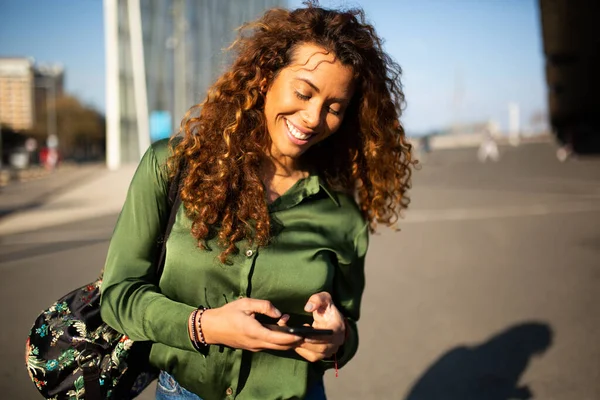 有魅力的年轻女子走在外面用手机看短信的画像 — 图库照片