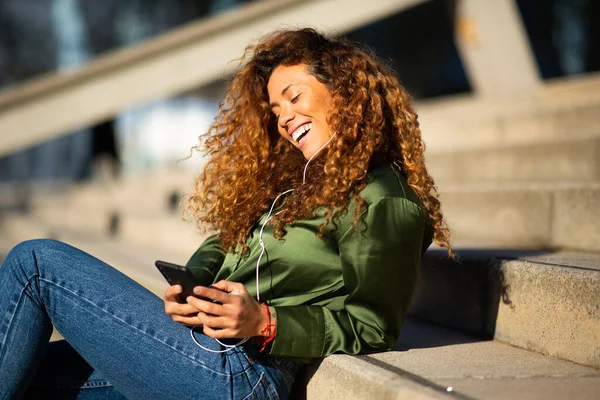 市の階段で携帯電話やヘッドフォンを使用して音楽を聞いて陽気な若い女性の肖像画 — ストック写真