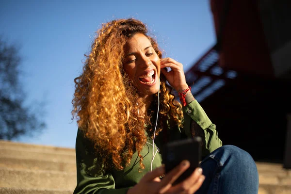 美しいラテン語の女性の肖像は イヤホンや携帯電話で音楽を聞いて楽しむ外のステップに座って — ストック写真