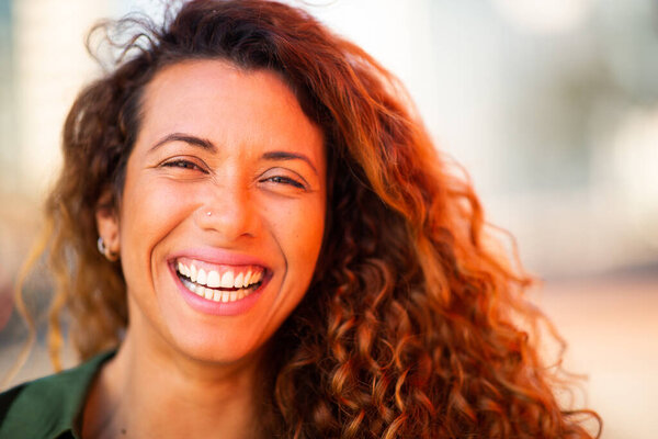 Close up portrait of smiling young hispanic woman looking at camera and laughing outside
